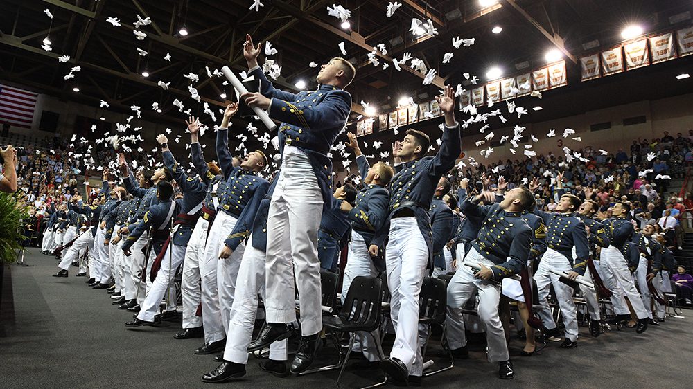 Graduating cadets jump and throw their gloves in the air.