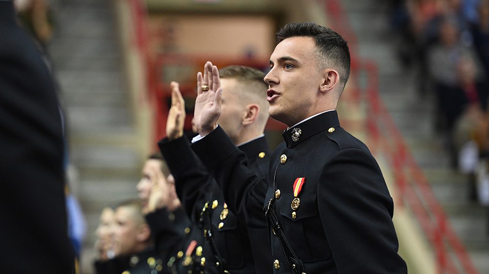 Men and women in Marine Corps uniforms stand with right hands raised