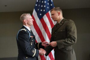 Michael Hoffman ’22 shakes hands with Col. David Gray in front of American flag.