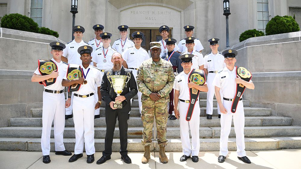 Members of Club Boxing Team post on steps of Smith Hall with Maj. Gen. Cedric Wins '85. They are all wearing medals, and some hold boxing belts and a trophy.
