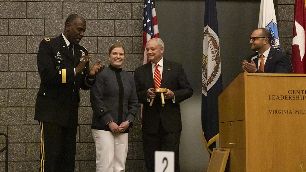 Makenna Moore smiles as Maj. Gen. Wins and Andrew Deal applaud her, and Bland Massie presents her with the Three-Legged Stool Award.