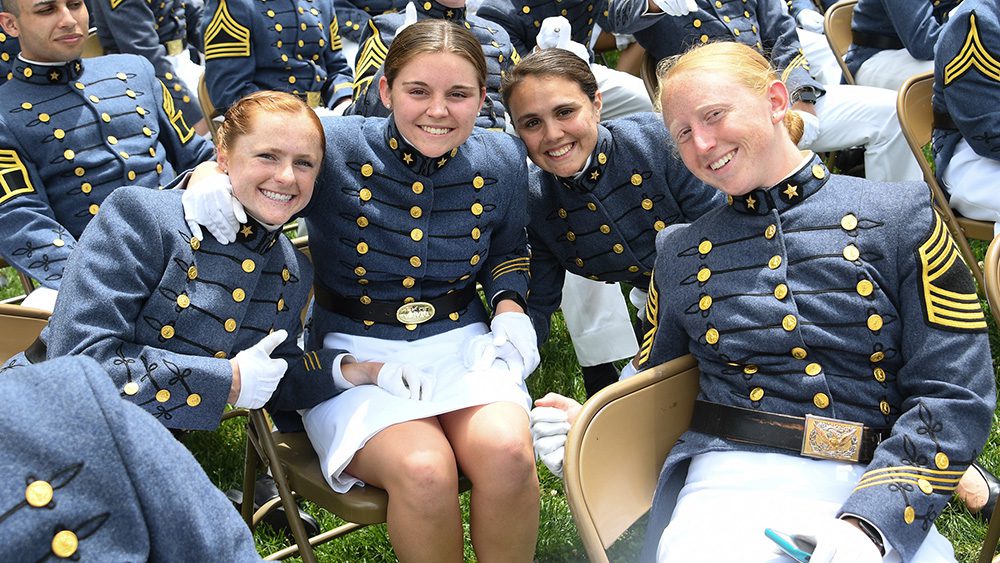Four female cadets seated, smiling, with arms around each other.