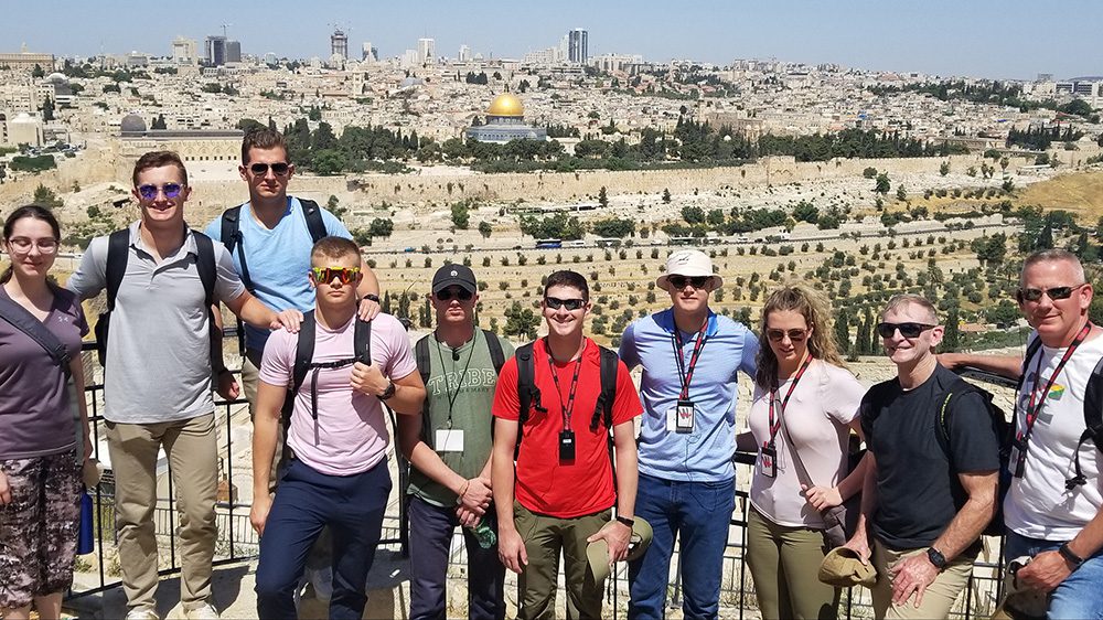 group of cadets and professor standing in a row smiling with Jerusalem skyline in background