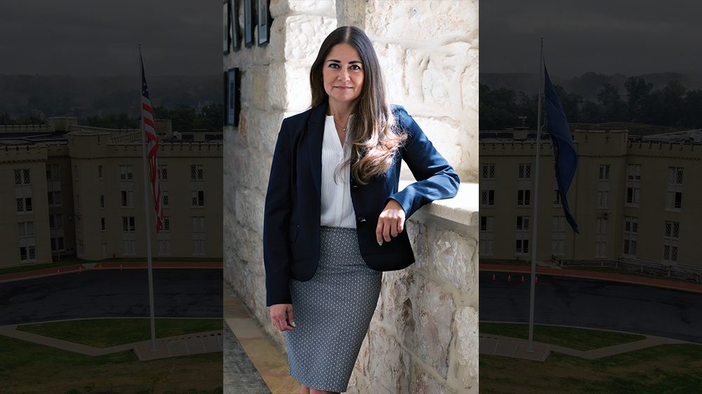 Col. Angelica Martinez '02, Ph.D. leaning against a wall smiling