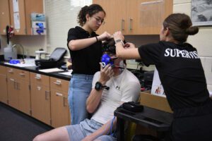 two people adjust mask and head strap on male subject before he enters hypoxic chamber.