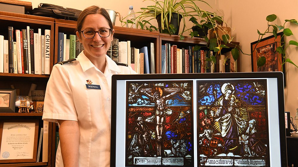 Lt. Col. Catharine Ingersoll poses with a photograph of the two 16th-century stained-glass panels.