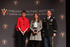 three people posing in front of "VMI" logo background, one holding an award