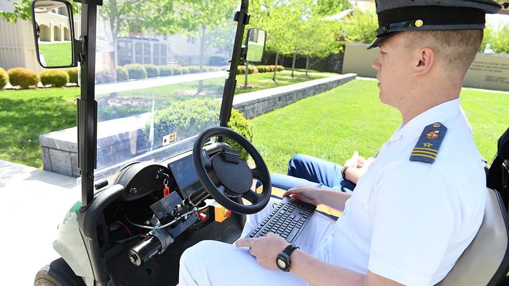 cadet sitting in golf cart with keyboard, driving computer-operated vehicle