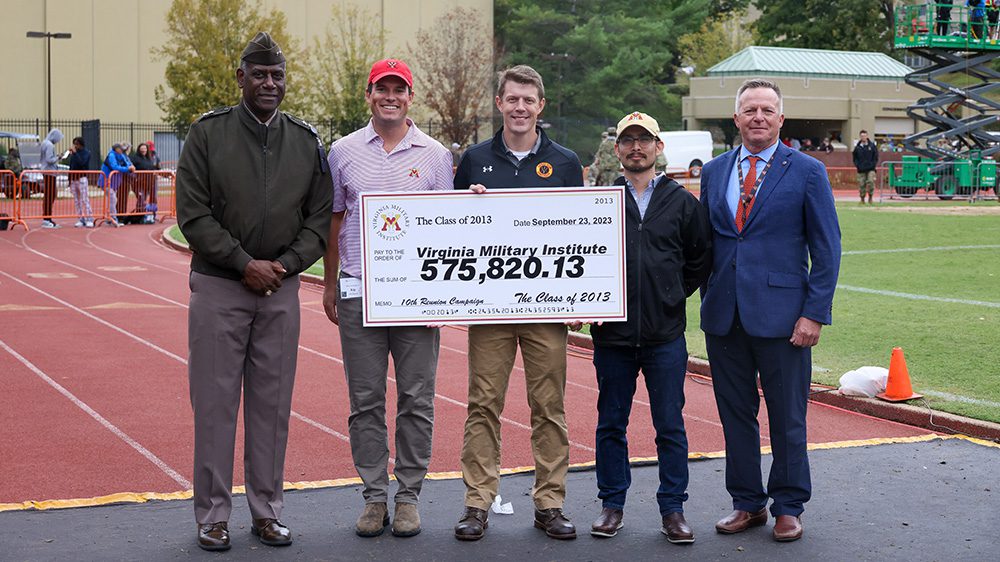 Maj. Gen. Cedric T. Wins ’85, superintendent; Kip Zechman ’13; Donnie Martin ’13; Dante Morales ’13; and David Prasnicki, VMI Alumni Agencies chief executive officer, holding a presentation check.