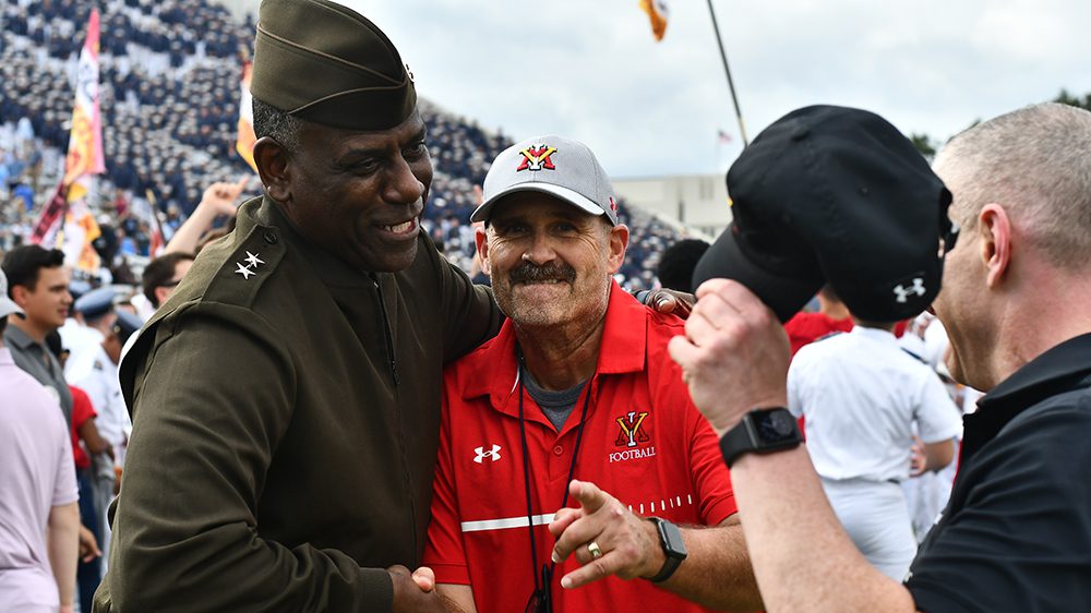 Maj. Gen. Cedric T. Wins '85, superintendent, smiling and shaking hands with Danny Rocco, head VMI football coach, as Rocco points at the camera and smiles