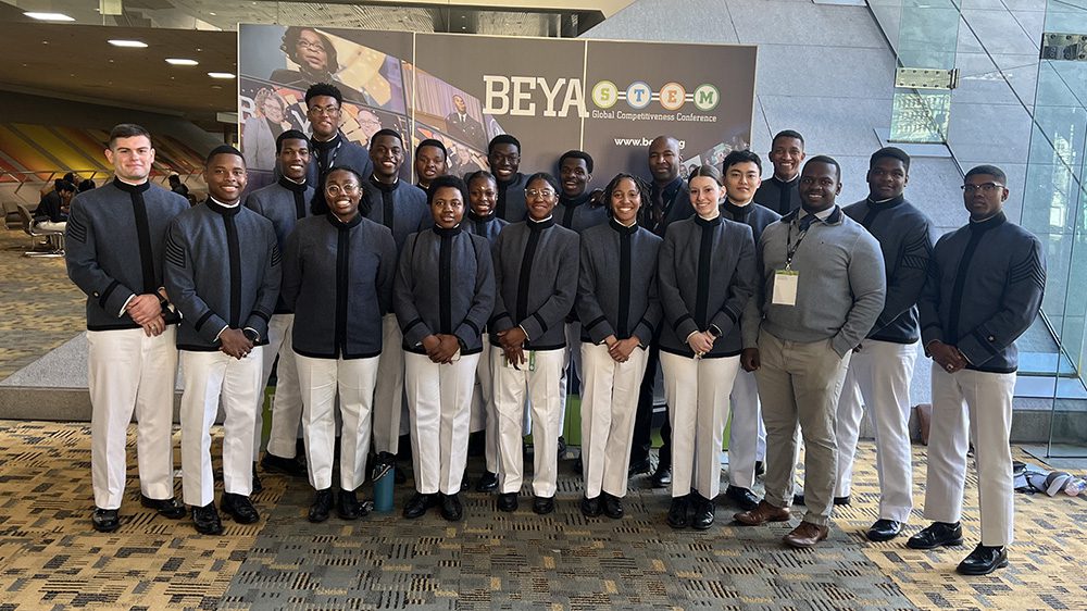 Cadets gathered in front of BEYA poster, smiling.