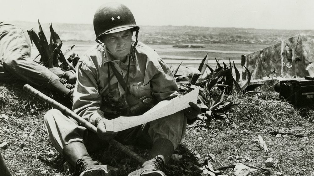 black and white photo of marine sitting on the ground reading a map