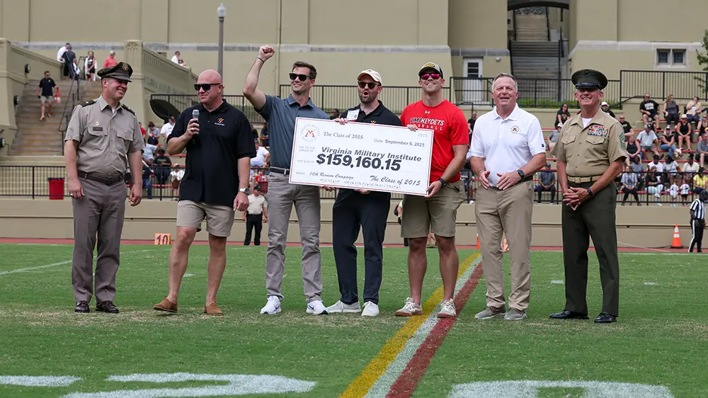 alumni hold large cardboard check on football field