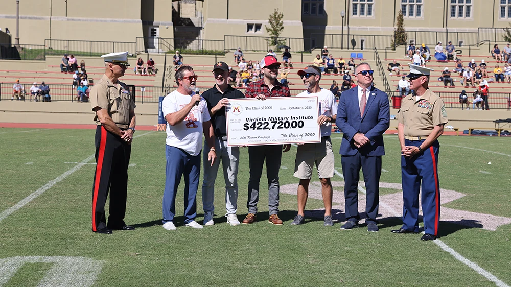 members of Class of 2000 holding giant cardboard check on football field
