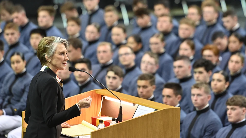Woman standing behind podium giving speech to audience full of cadets