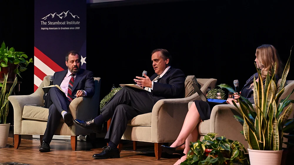 three people sitting in chairs having a debate on stage
