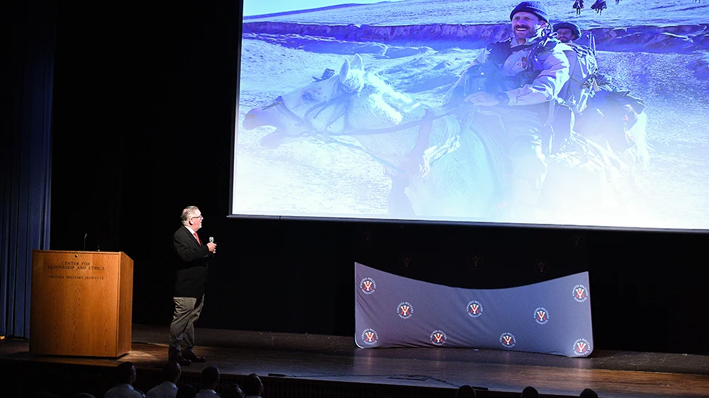 man giving presentation on stage with photo projected behind him