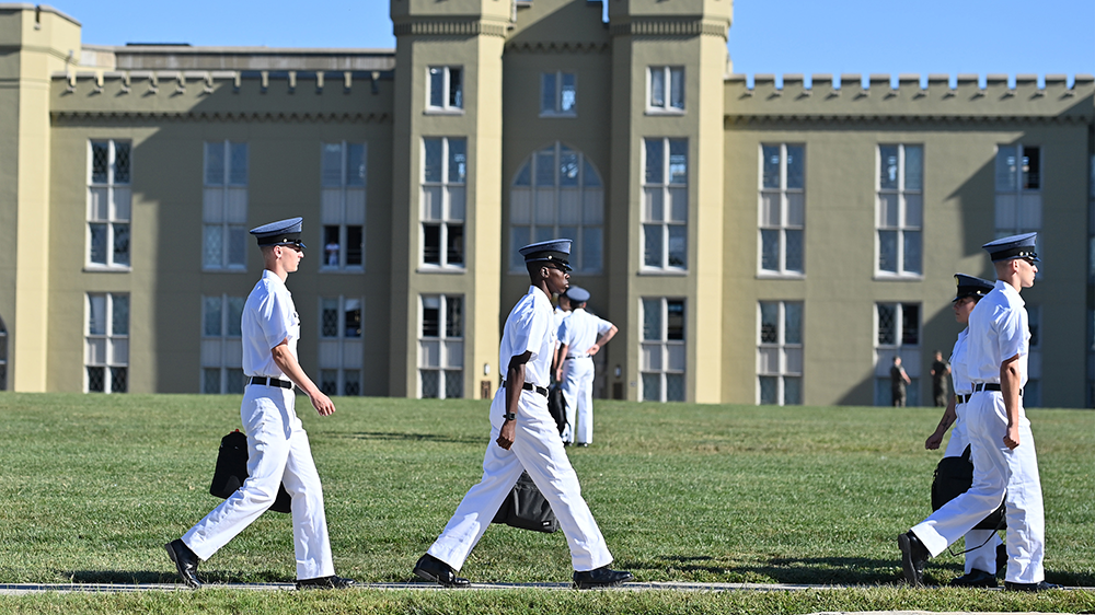 cadets walking with laptop bags, barracks in background